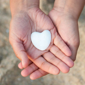 Hand holding a stone heart on the beach. Symbol of life.
